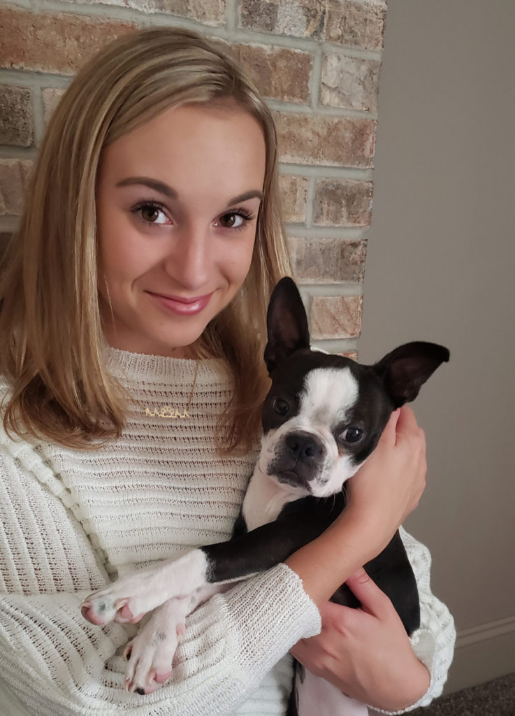 Furbeat brand pet jewelry shows model wearing a necklace with her pet's heartbeat while holding her boston terrier puppy.
